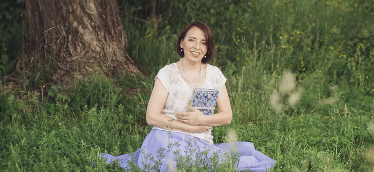 Психолог Ольга Овчинникова, автор колоды МАК-карт «Народная кукла», сидит на траве.