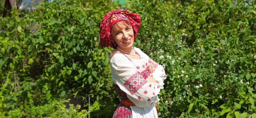 Психолог Ольга Овчинникова в народном костюме улыбается на фоне летней зелени.